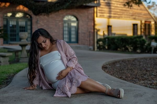 Pregnant woman sitting on the ground in a courtyard, looking down naturally rather than posing for the camera