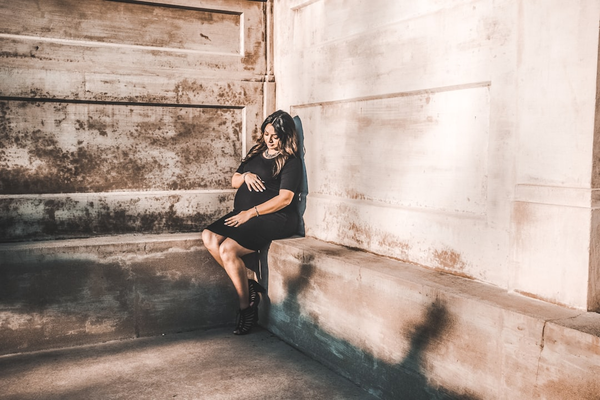Pregnant woman leaning back against a stone wall, eyes closed, relaxed and not looking at the camera