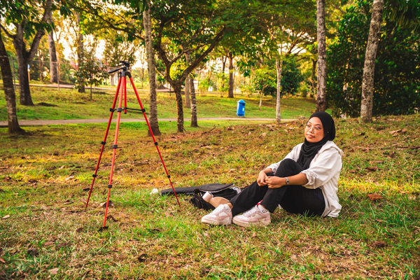 Tripod set up in a park, with a person seated nearby preparing for a self-timer photo
