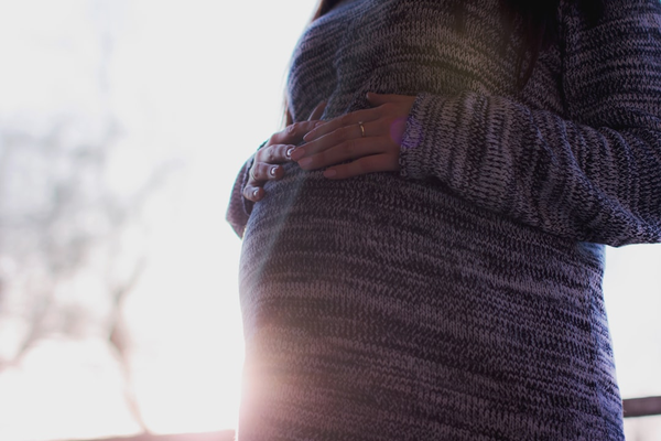 Close-up of hands resting on a pregnant belly in a cozy knit sweater, warm natural light